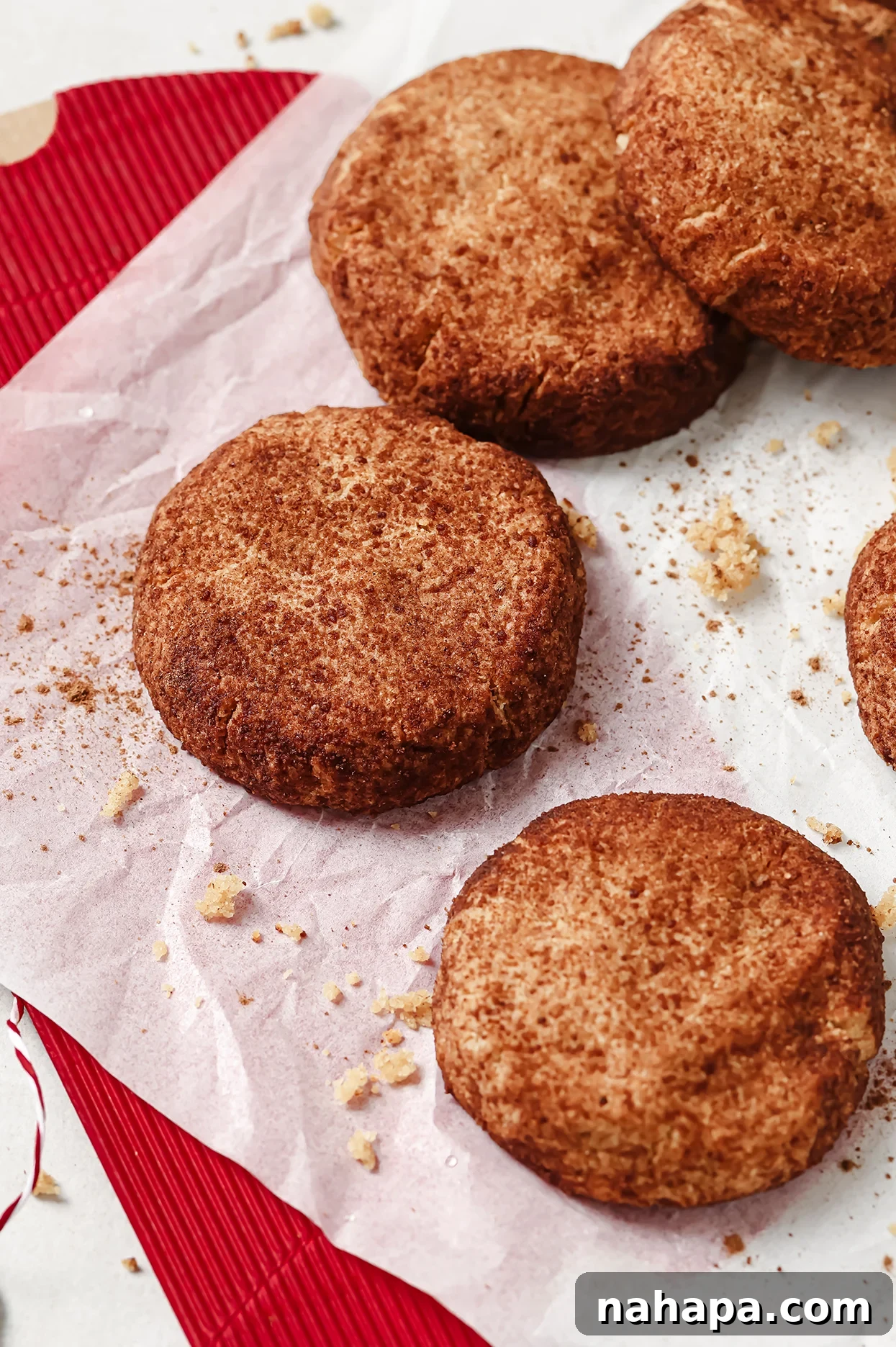 A close-up of gluten-free Snickerdoodle cookies on a baking tray, showing their crinkled tops, cinnamon sugar coating, and some scattered crumbs.