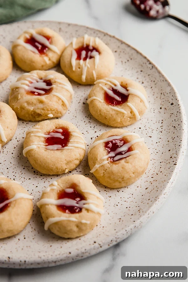 Classic gluten-free thumbprint cookies adorned with vibrant jam and a delicate coconut butter drizzle, presented on a white plate