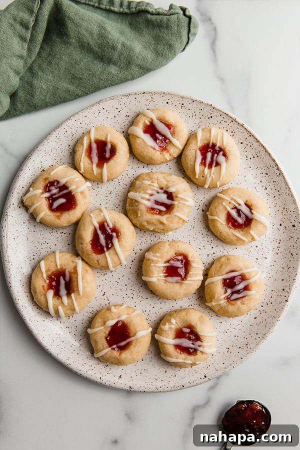 A festive plate of gluten-free thumbprint cookies, each with a vibrant jam filling and a delicate white drizzle, ready for holiday serving