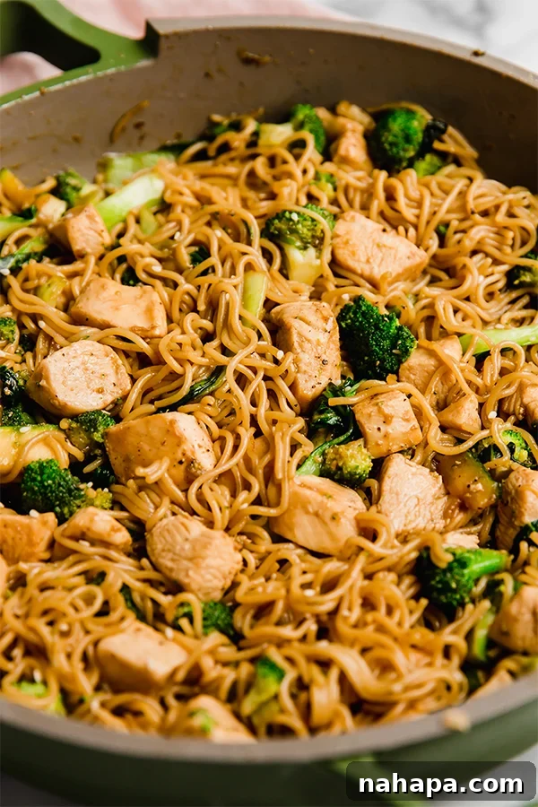 Close-up shot of chicken and ramen stir fry in a bowl, showing the texture of the noodles, chicken, and colorful vegetables.
