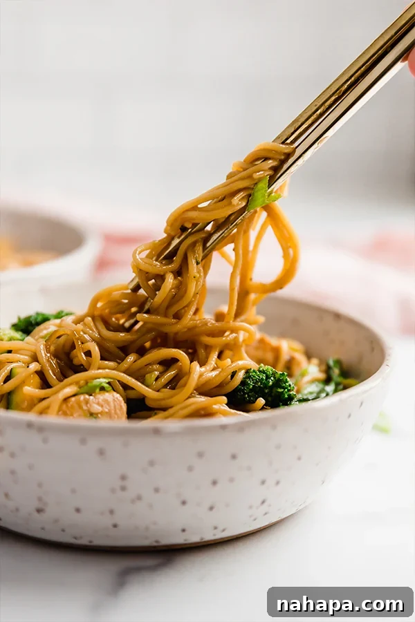 Chicken and ramen stir fry being eaten with chopsticks, highlighting its appetizing nature.
