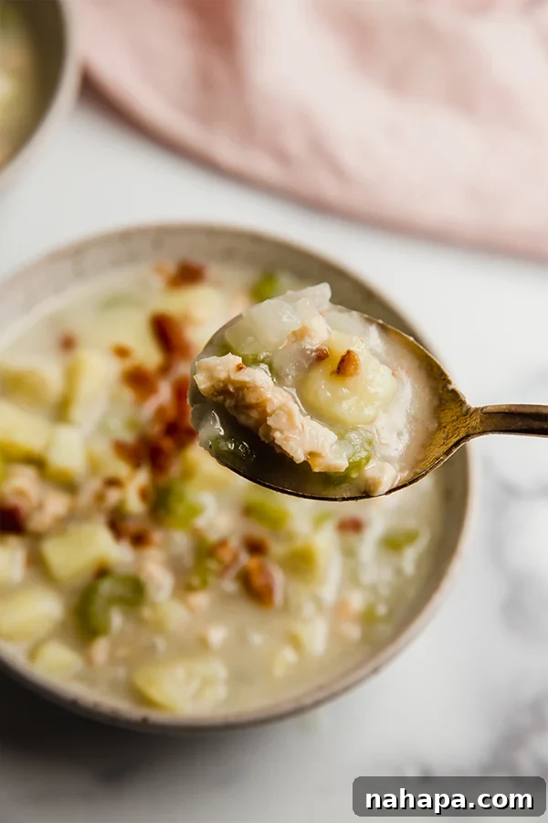 A close-up of a spoonful of clam chowder being lifted from the bowl, highlighting its rich texture and chunks of clam.