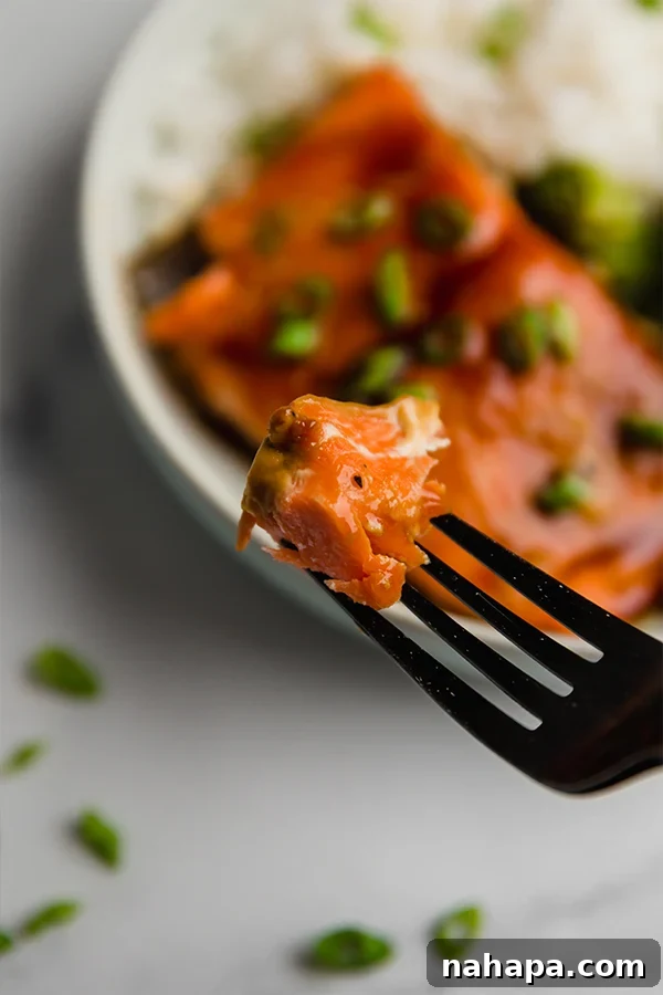 bite of teriyaki salmon on fork with bowl in background