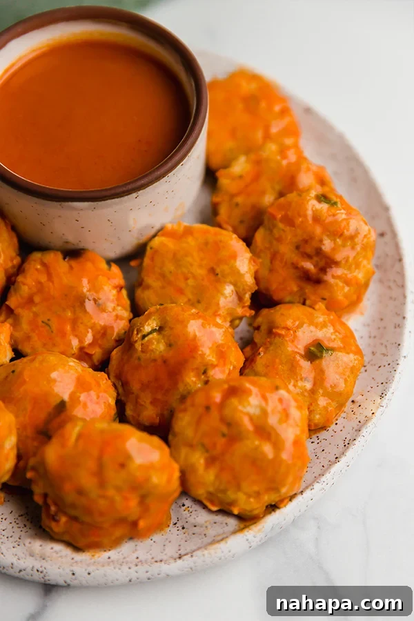 Delicious Buffalo Chicken Poppers artfully arranged on a serving plate with a generous drizzle of spicy sauce.
