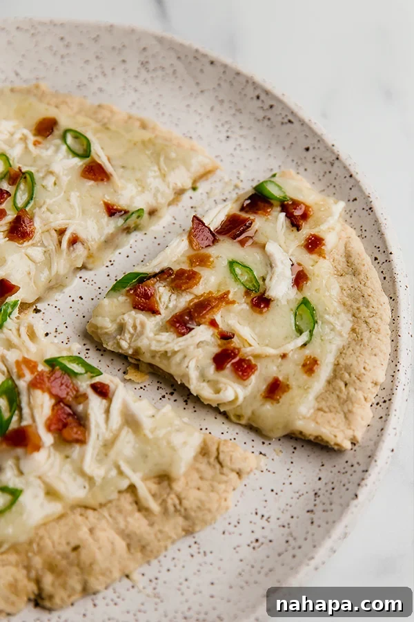 A whole AIP & Paleo Chicken Bacon Ranch Pizza on a plate, with a slice removed, showcasing its delicious layers