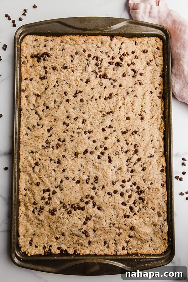 A freshly baked sheet pan chocolate chip cookie, still warm on the baking pan, ready to be sliced and enjoyed.