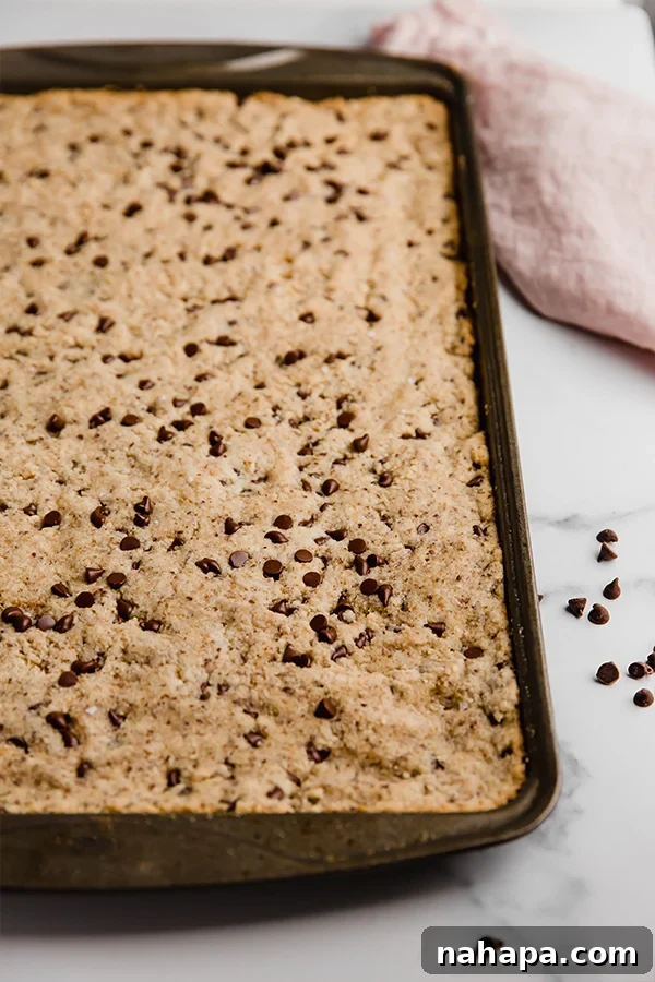 A large, rustic sheet pan chocolate chip cookie, freshly baked and still in the pan, waiting to be enjoyed.