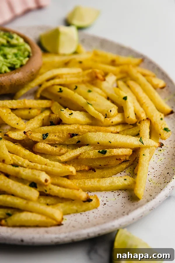 Close-up of golden brown jicama fries piled on a plate, garnished with fresh cilantro, next to a bowl of creamy guacamole.