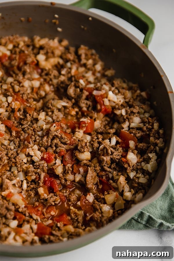 Ground beef and cauliflower rice mixture being sautéed in a large pan with diced onions and spices