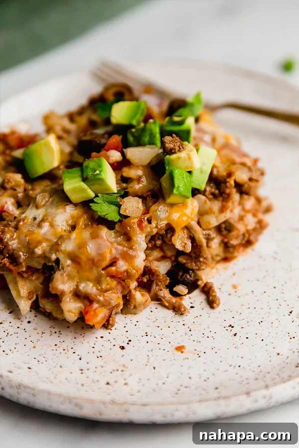 A single serving of taco cauliflower rice casserole on a white plate, garnished with fresh cilantro and avocado slices