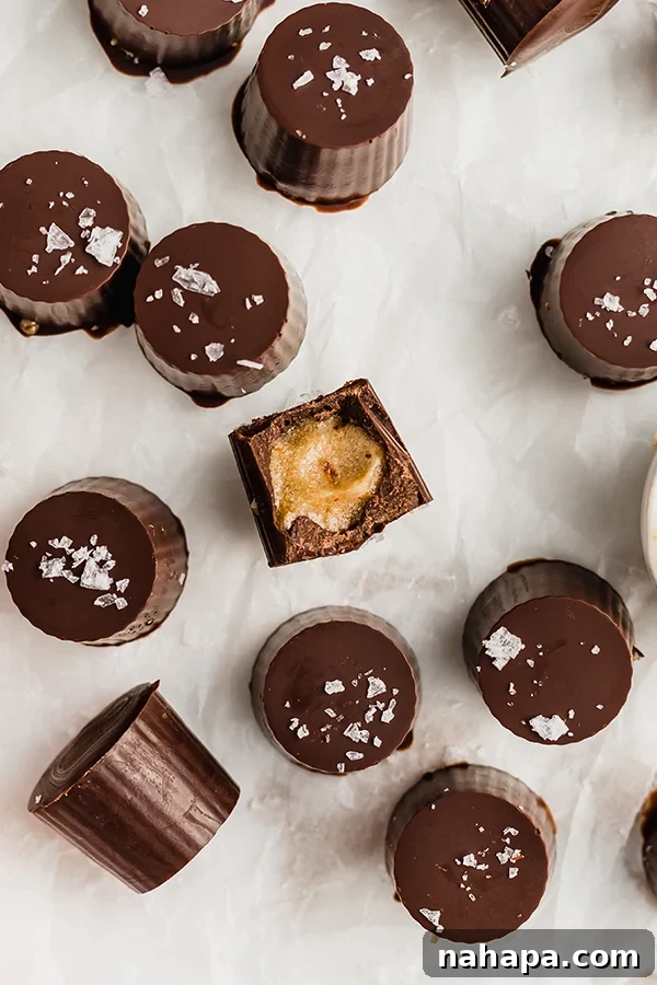 A close-up of a single salted caramel cup, showing the gooey date caramel filling and chocolate shell, topped with flaky salt.