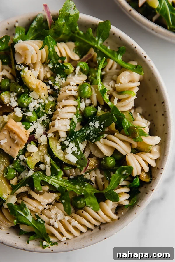 A beautifully presented spring pasta salad with gluten-free pasta, chicken, and fresh vegetables in a rustic bowl.