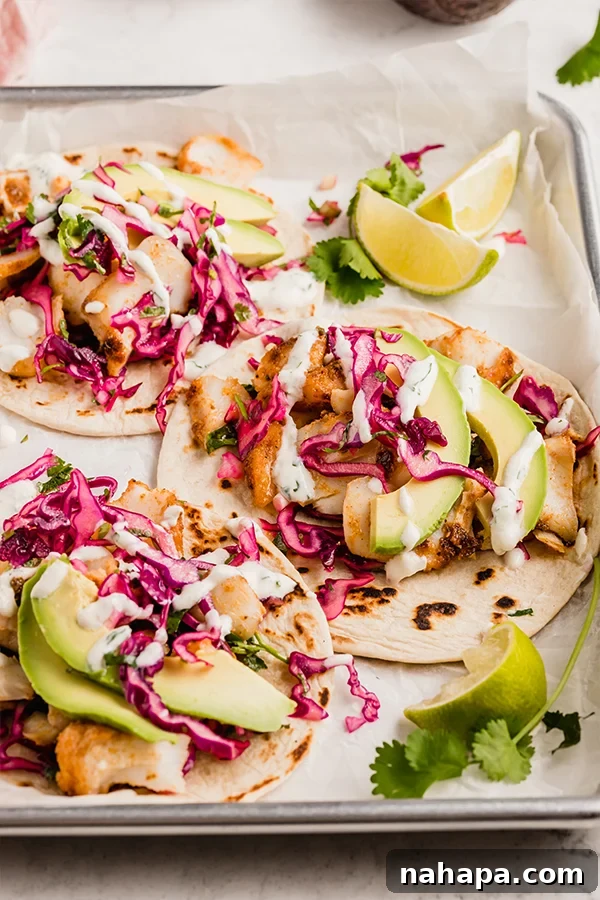 Effortless Fish Tacos with Zesty Slaw 5 Three fully assembled fish tacos on a wooden serving tray, garnished with fresh cilantro, lime, and a side of creamy sauce.