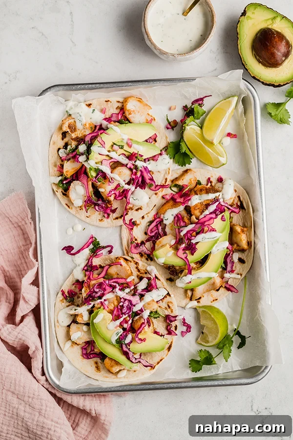 Effortless Fish Tacos with Zesty Slaw 6 Three fish tacos on a tray with fresh avocado slices, lime wedges, cilantro, and a small bowl of creamy sauce.