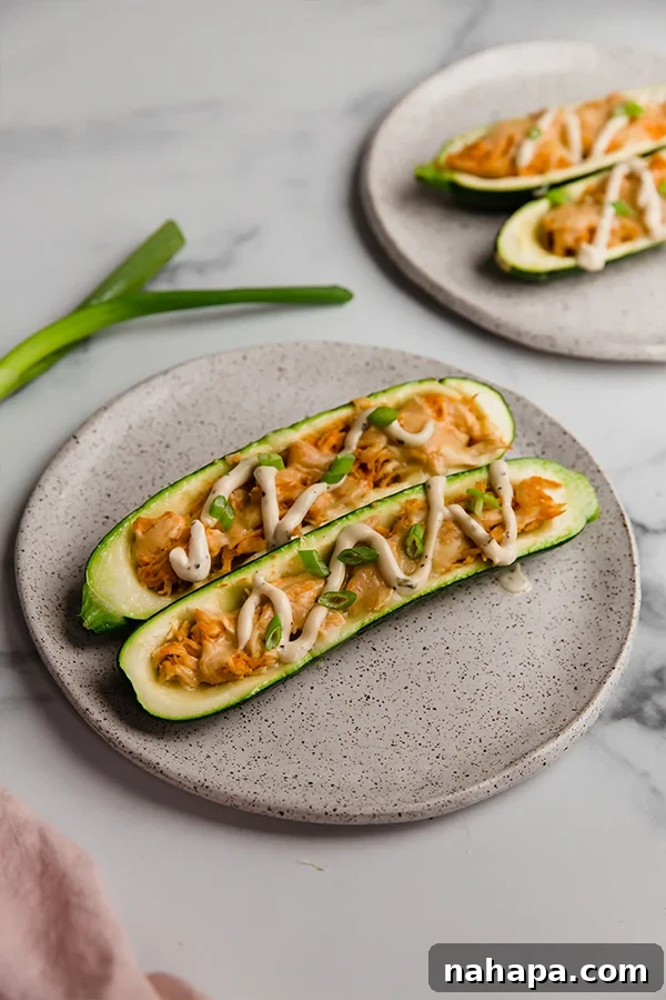 A perfectly cooked buffalo chicken stuffed zucchini boat, plated and ready to eat, topped with ranch and green onions