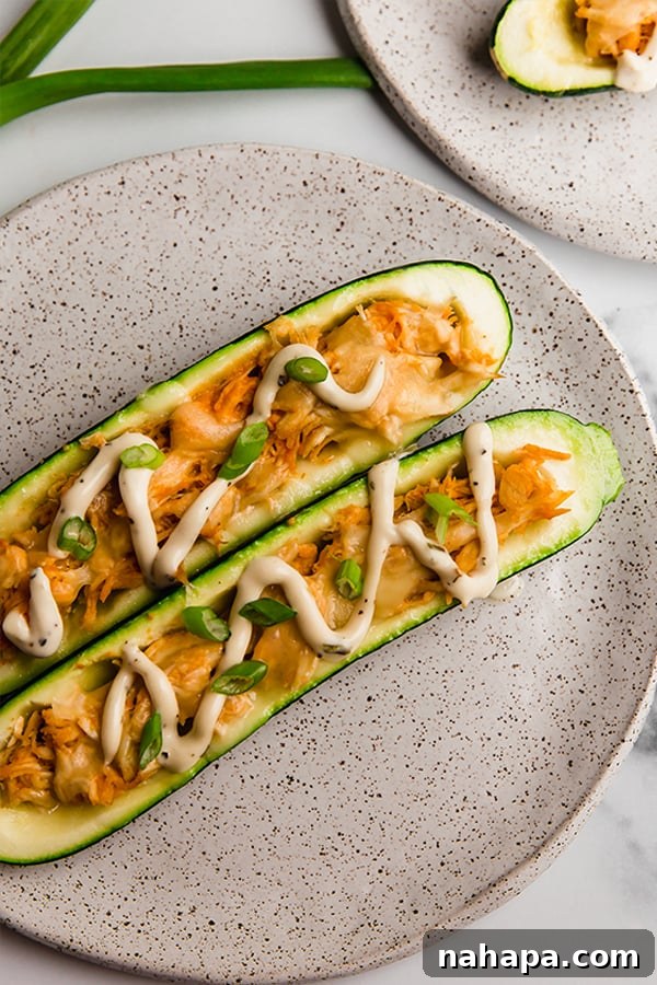 Close up image of the finished buffalo chicken stuffed zucchini boat on a plate, showing the texture of the chicken and melted cheese