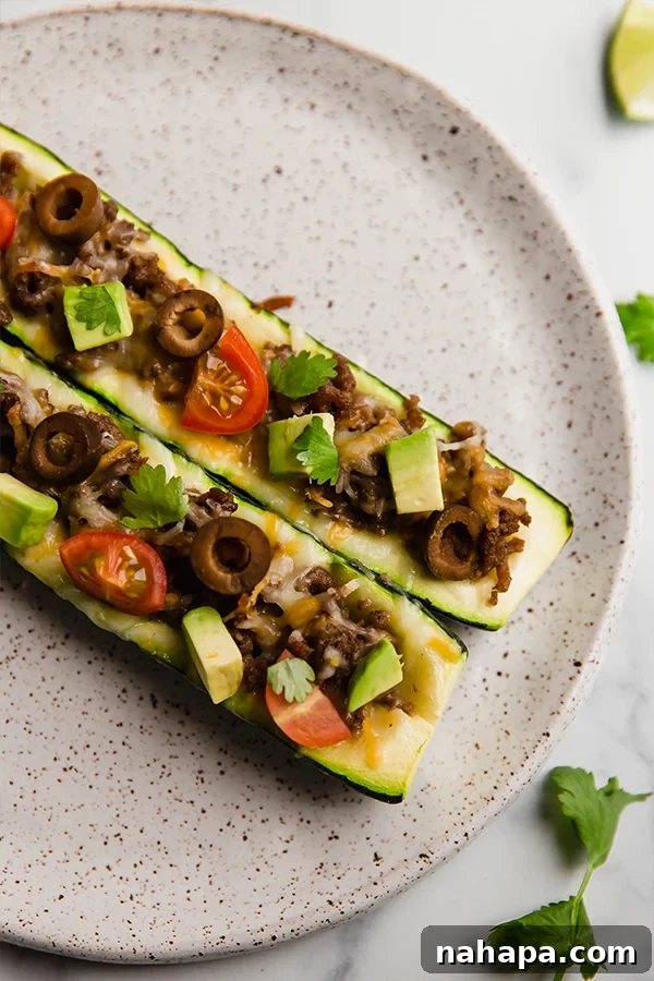 Savory Zucchini Taco Boats Low Carb Paleo Whole30 AIP 2 Two perfectly cooked taco stuffed zucchini boats, beautifully plated and garnished with fresh avocado slices, cherry tomatoes, and cilantro, highlighting their vibrant appeal and healthy nature.