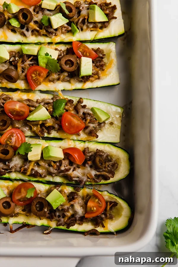 Savory Zucchini Taco Boats Low Carb Paleo Whole30 AIP 5 An inviting close-up view from above shows multiple taco stuffed zucchini boats in a baking dish, highlighting the rich filling and fresh, colorful toppings, ready to be enjoyed.