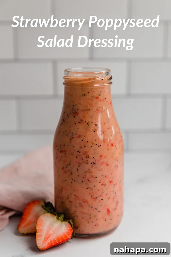A small bowl of homemade strawberry poppyseed dressing, bright pink with visible poppy seeds, next to fresh strawberries.