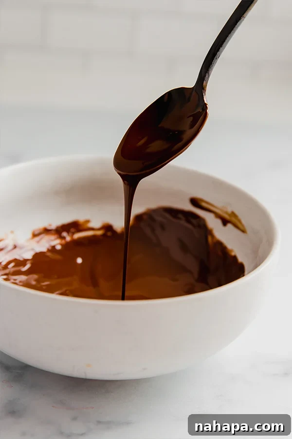 Melted dairy-free chocolate dripping from a spoon, prepared for glazing.