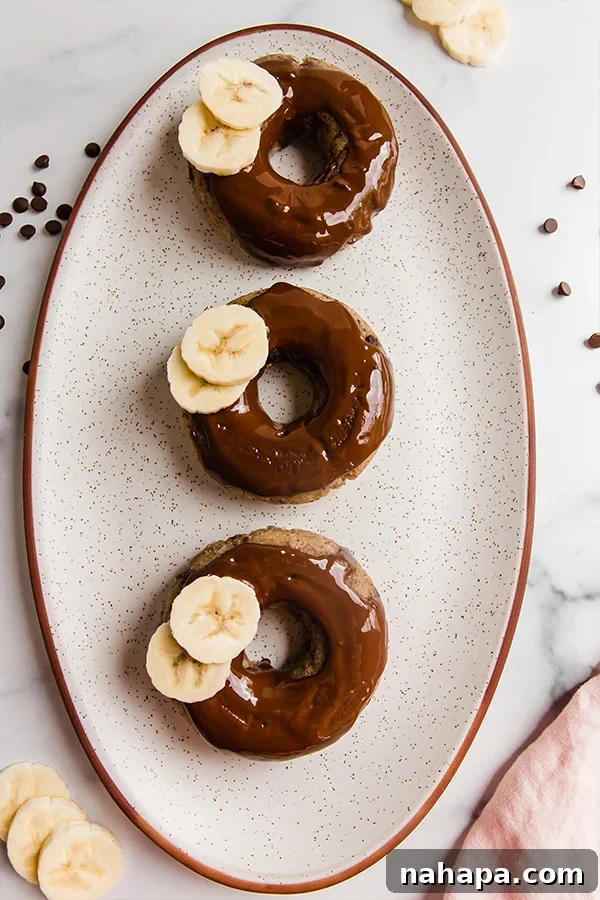 Three perfectly baked banana bread donuts resting on a white plate, ready to be enjoyed.
