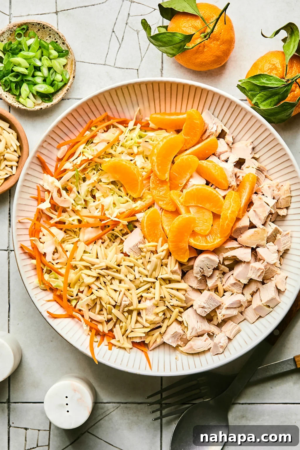 Coleslaw mix, shredded carrots, slivered almonds, mandarin orange segments, and cubed chicken combined in a large mixing bowl