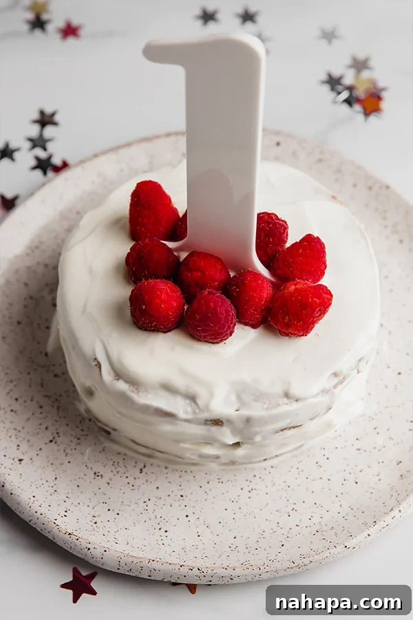 Beautifully frosted sugar-free baby smash cake adorned with fresh, vibrant raspberries, ready for a baby's first birthday celebration.