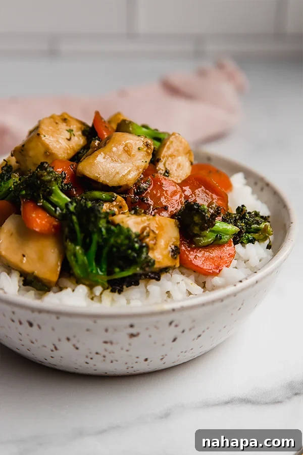 Up close view of chicken stir fry in bowl, showcasing the glossy sauce and fresh vegetables