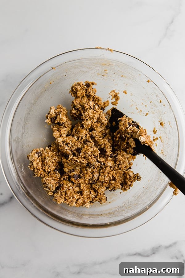 All the ingredients for the energy bites mixed together in a clear glass bowl with a spatula, showing the sticky texture before rolling.