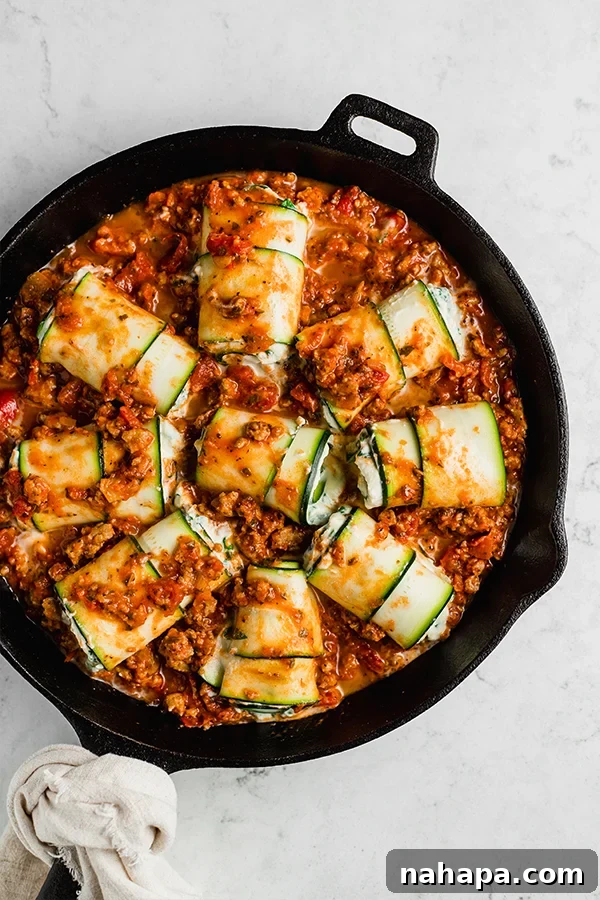Top view of zucchini roll ups arranged in a cast iron pan with meat sauce, ready for baking