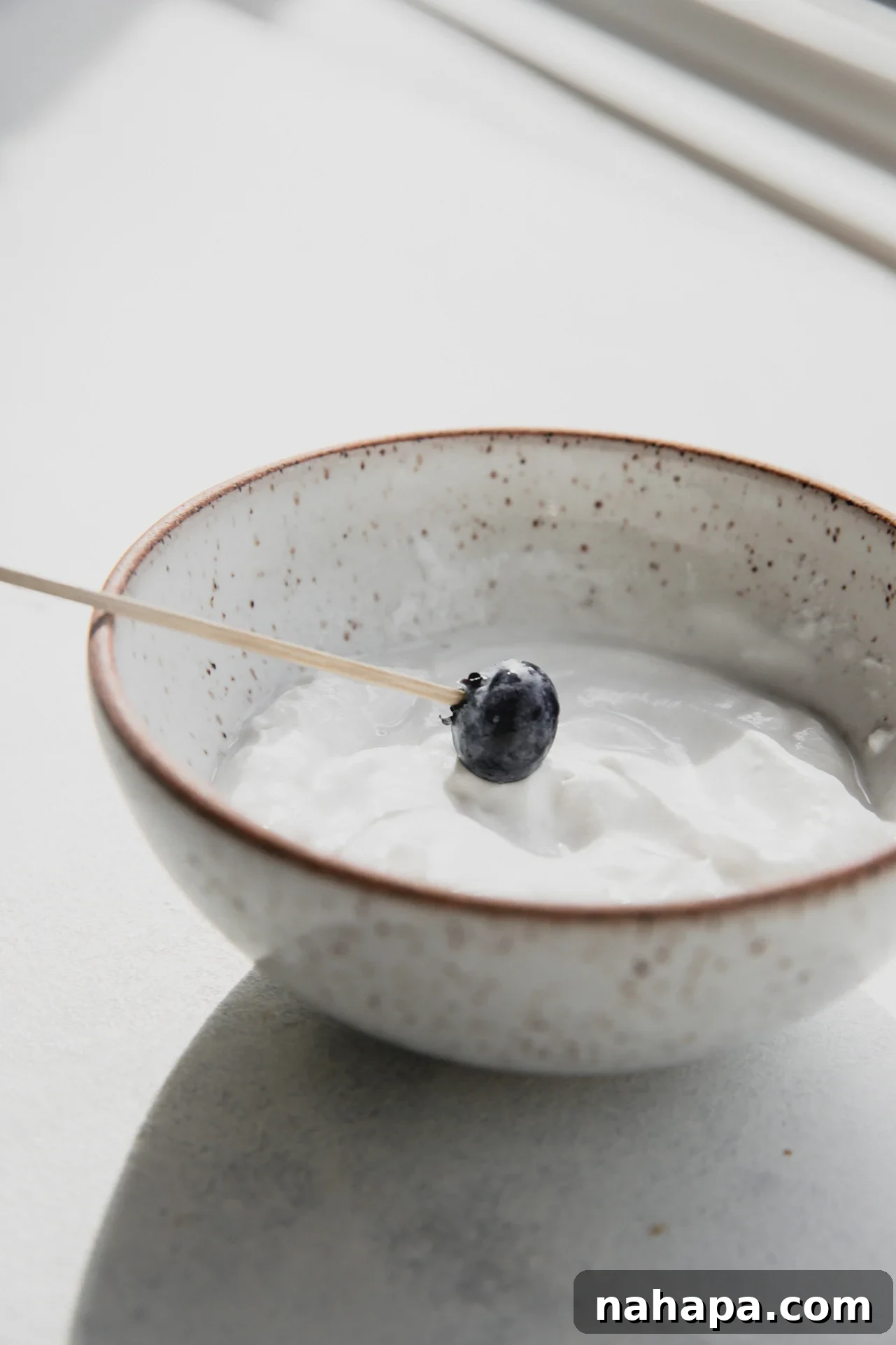 Blueberry on a toothpick dipping in yogurt.