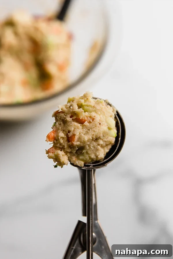 Veggie muffin batter being scooped into a mini muffin pan before baking.