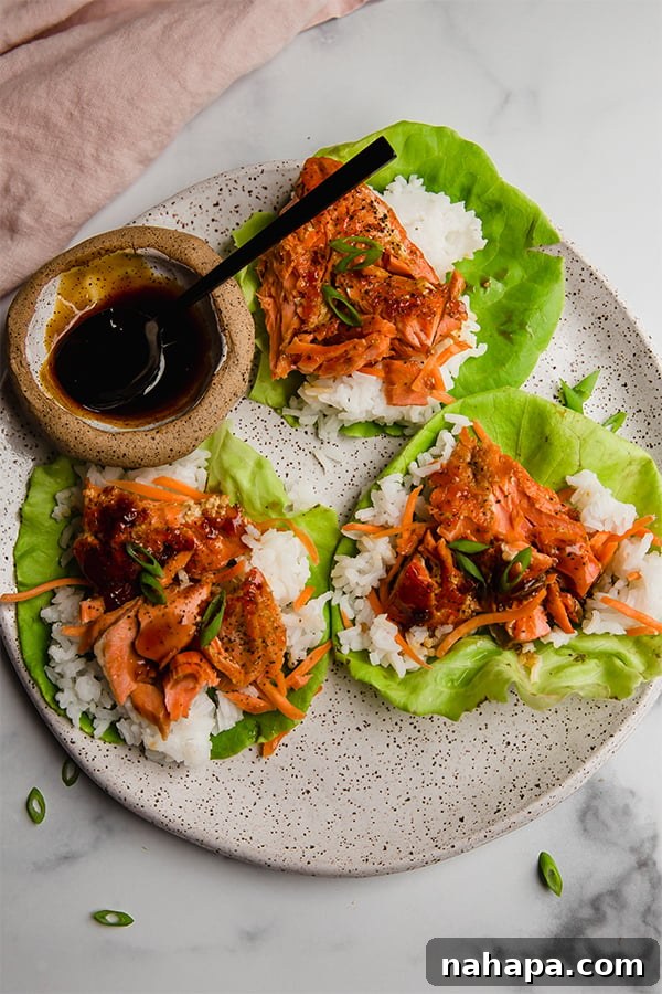 A trio of salmon lettuce cups displayed on a white plate, accompanied by a small bowl of teriyaki sauce, highlighting the complete and inviting meal.