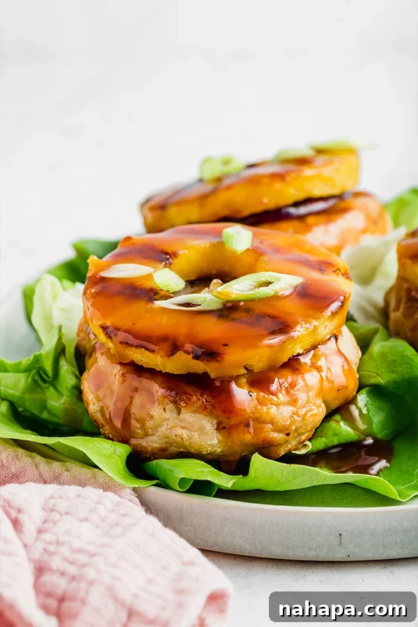 Up close side view of a perfectly grilled chicken burger with a caramelized pineapple ring on top, served on lettuce
