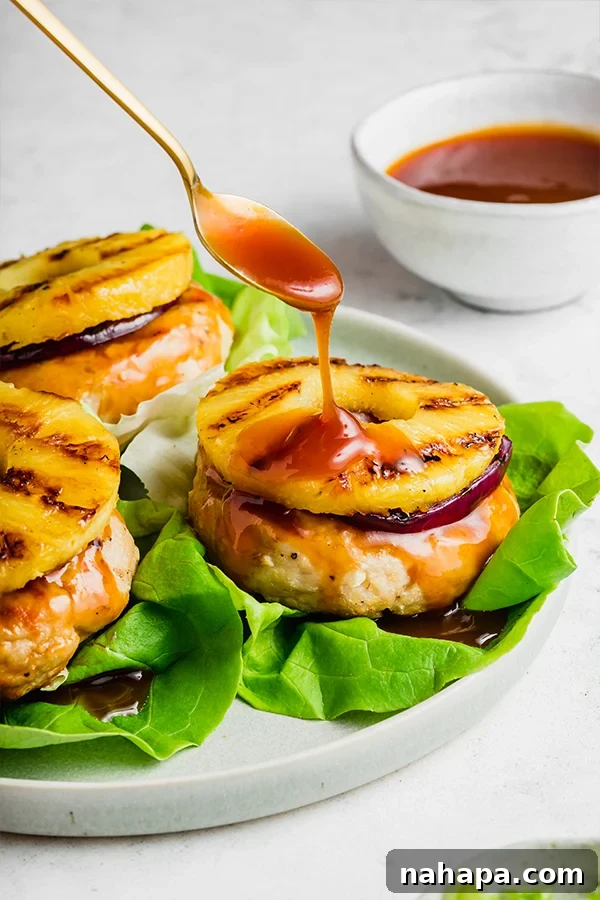 Chicken burgers on a plate with a spoon drizzling sweet and sour sauce over top, showing the glistening texture