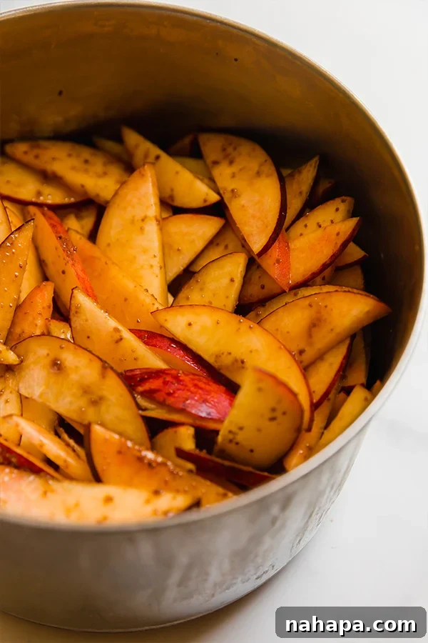 A close-up view of a metal pot filled with sliced peaches, gently cooking in a sweet, syrupy mixture on the stove, ready for the cobbler filling.