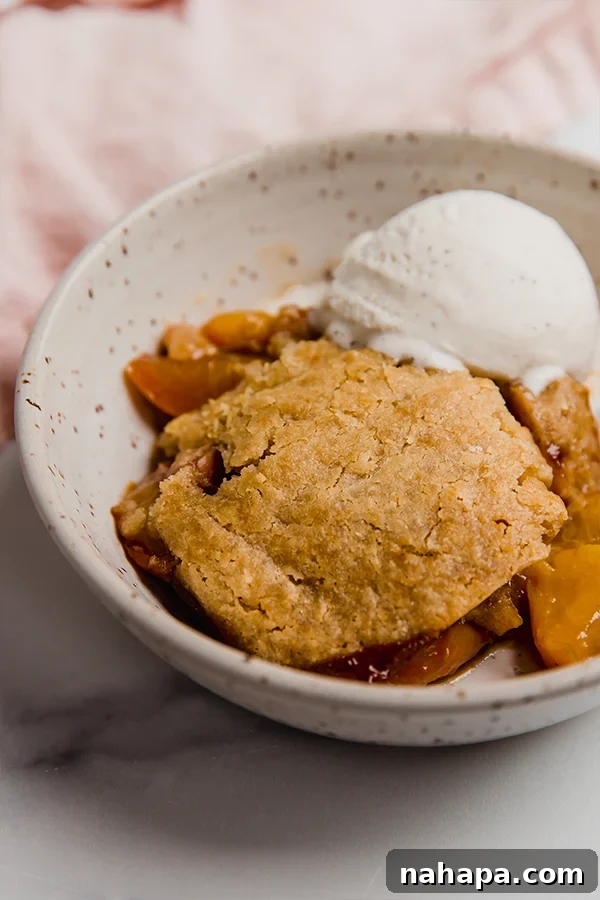 A vibrant, close-up shot of the Paleo and AIP Peach Cobbler, showcasing its golden biscuit topping and bubbling fruit filling, presented in a rustic, inviting style.