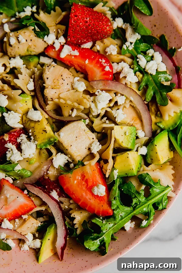 An up-close view of the strawberry balsamic pasta salad, highlighting the vibrant colors and fresh ingredients in a pink bowl.