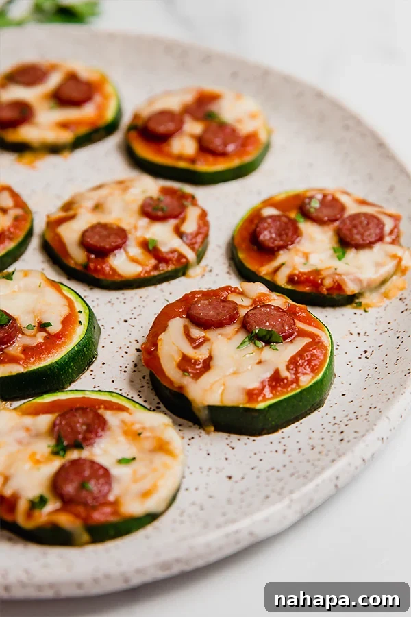 Close-up of baked Mini Zucchini Pizza Bites garnished with fresh parsley, presented on a white plate, ready to be enjoyed.