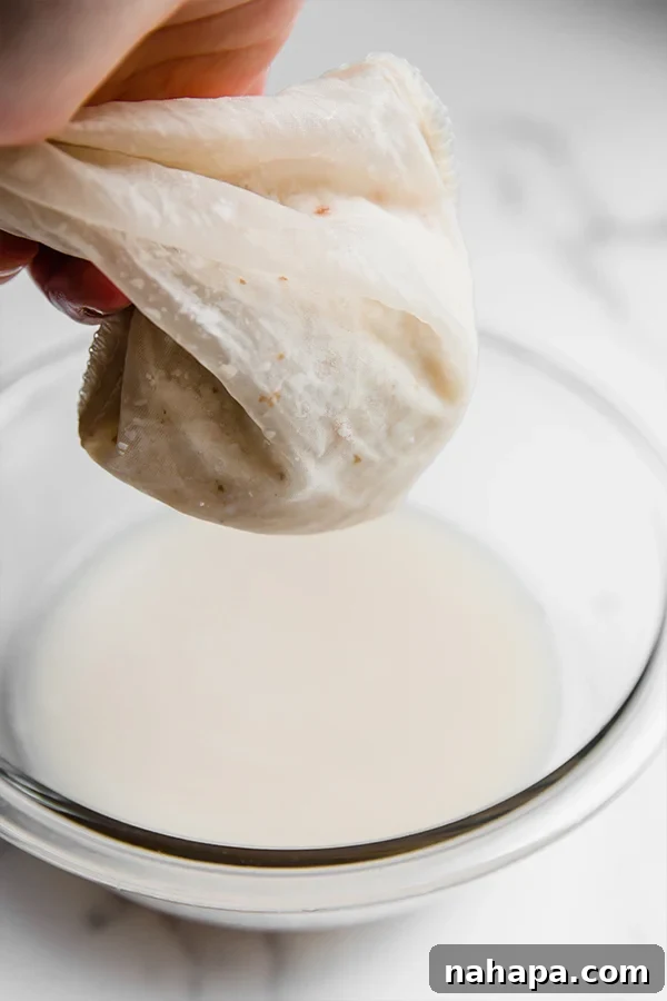 Straining coconut milk through a nut milk bag into a bowl.