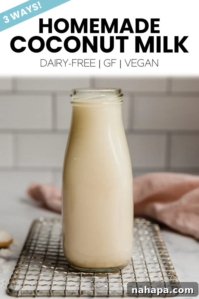 A glass jar of homemade coconut milk with a straw, next to a coconut cut in half.