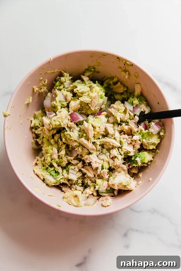 Wholesome Avocado Tuna Cucumber Boats for Clean Eating 3 Ingredients for tuna salad mixed together in a bowl, showing creamy avocado and flaky tuna.