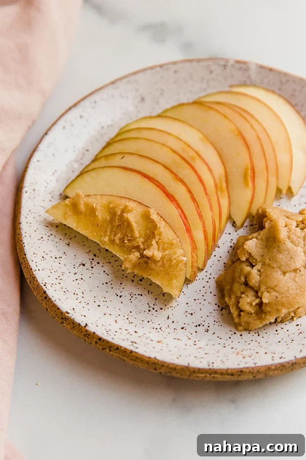 Kendi Kaplan Cevizi Ezmeni Kendin Yap! 5 Freshly sliced apples arranged on a plate, perfectly paired with a small bowl of creamy tigernut butter for a healthy and appealing snack.