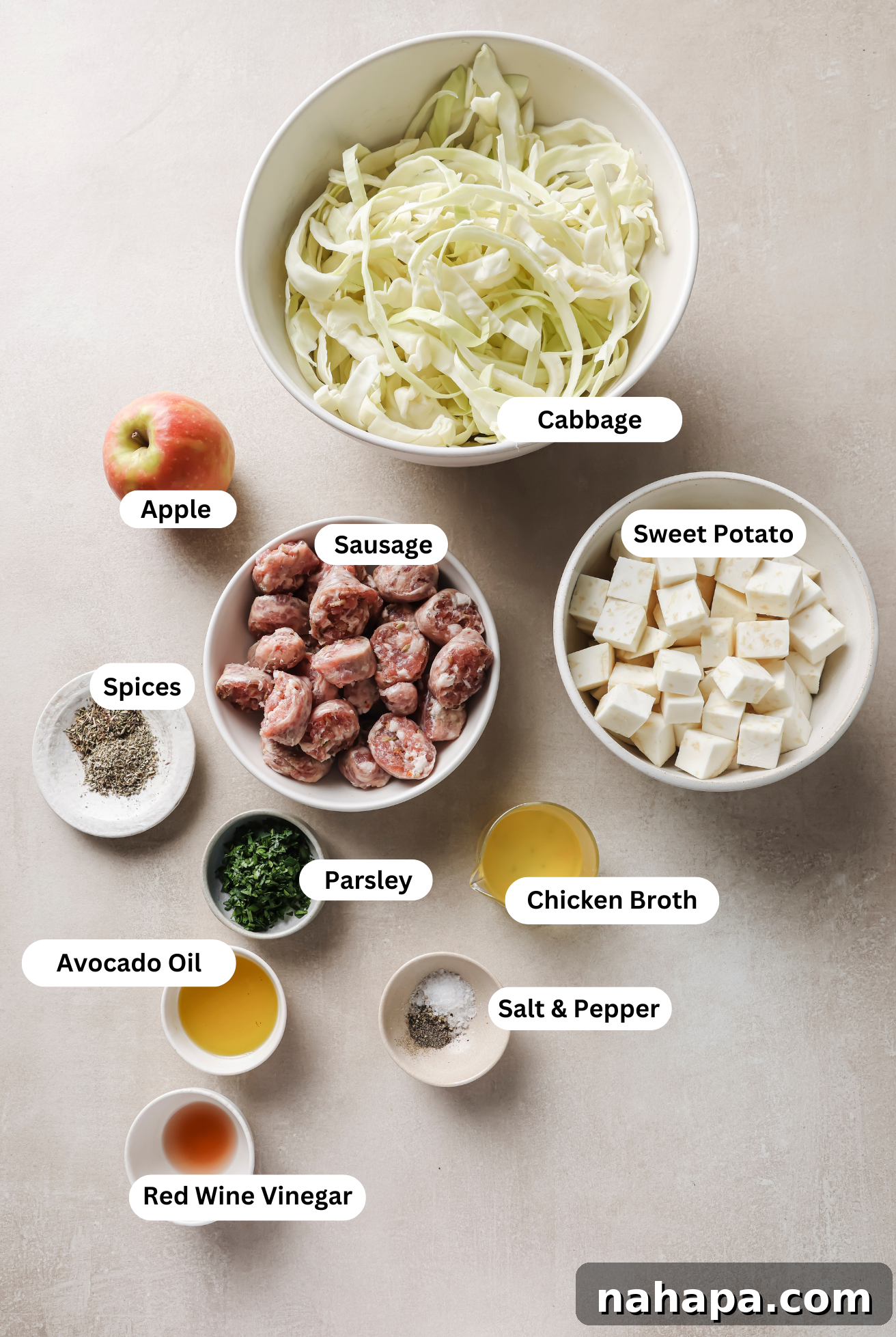All the fresh ingredients for the cabbage and sausage breakfast skillet neatly laid out on a wooden cutting board before cooking, including cubed sweet potatoes, sliced sausage, diced apple, shredded cabbage, and fresh parsley.