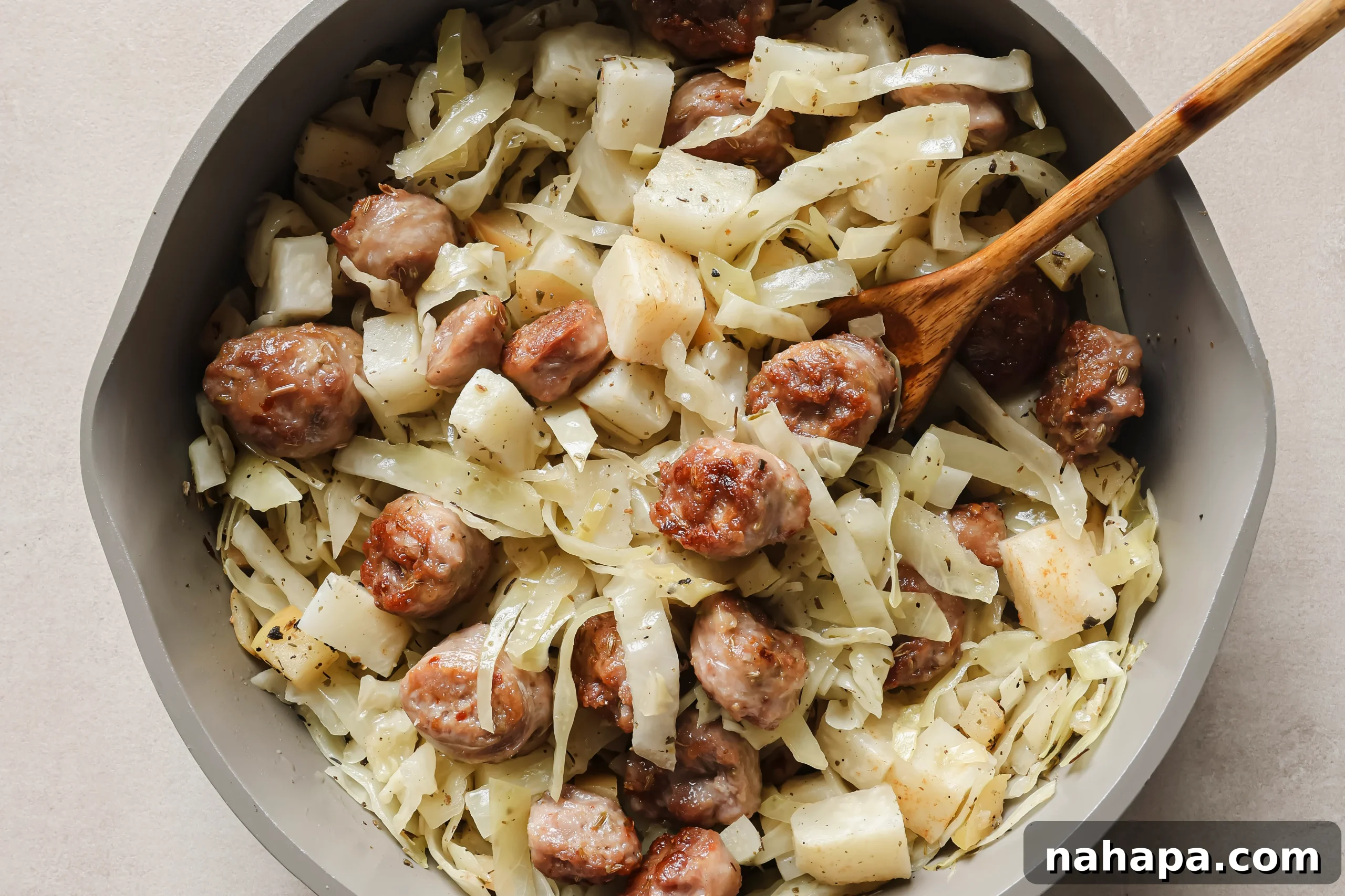 All the cooked ingredients, including sausage, sweet potatoes, cabbage, and apples, combined and stirred together in the pan, ready to be seasoned.