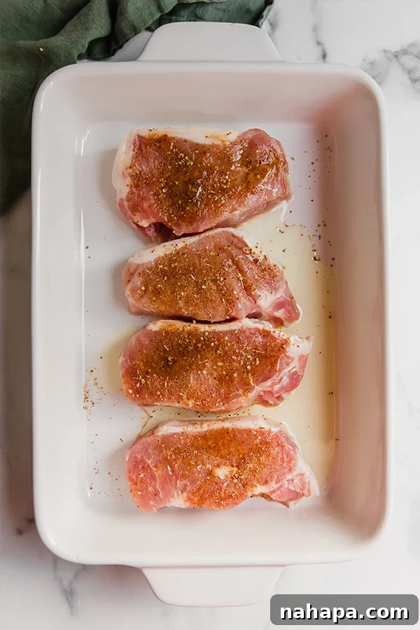 Four boneless pork chops, richly seasoned with a homemade spice rub, arranged neatly in a baking dish, ready to be transferred to the oven.