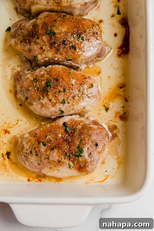 Golden-brown baked pork chops resting in a ceramic baking dish, showing their crispy exterior and inviting aroma.