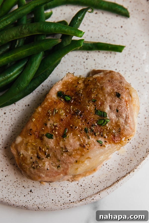 A perfectly baked pork chop, sliced and served with a side of green beans on a white plate, highlighting a well-balanced and appealing meal.