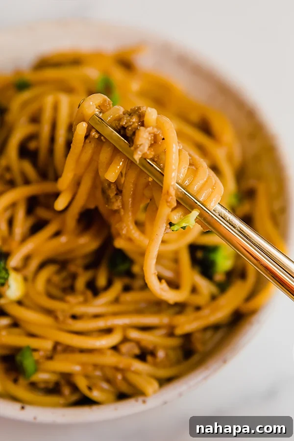 Close-up of Mongolian ground beef with noodles and broccoli in a white bowl, garnished with green onions, ready to eat