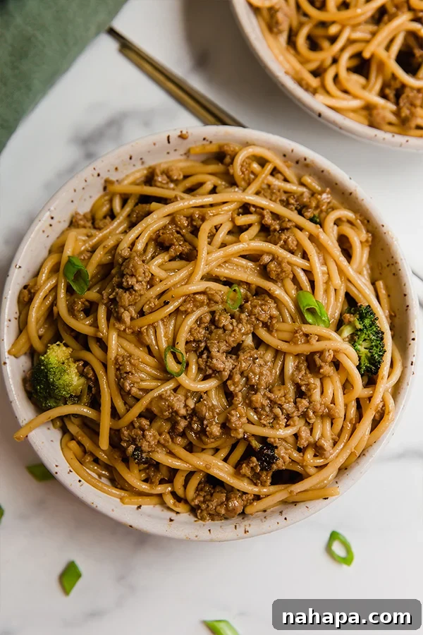 Top-down view of Mongolian ground beef with noodles and broccoli in a bowl, garnished with green onions and chopsticks